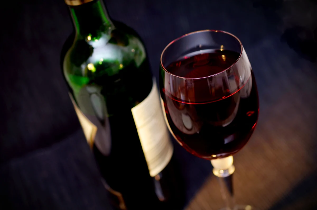 Bouteille de vin rouge et verre servi, posés sur une table sombre