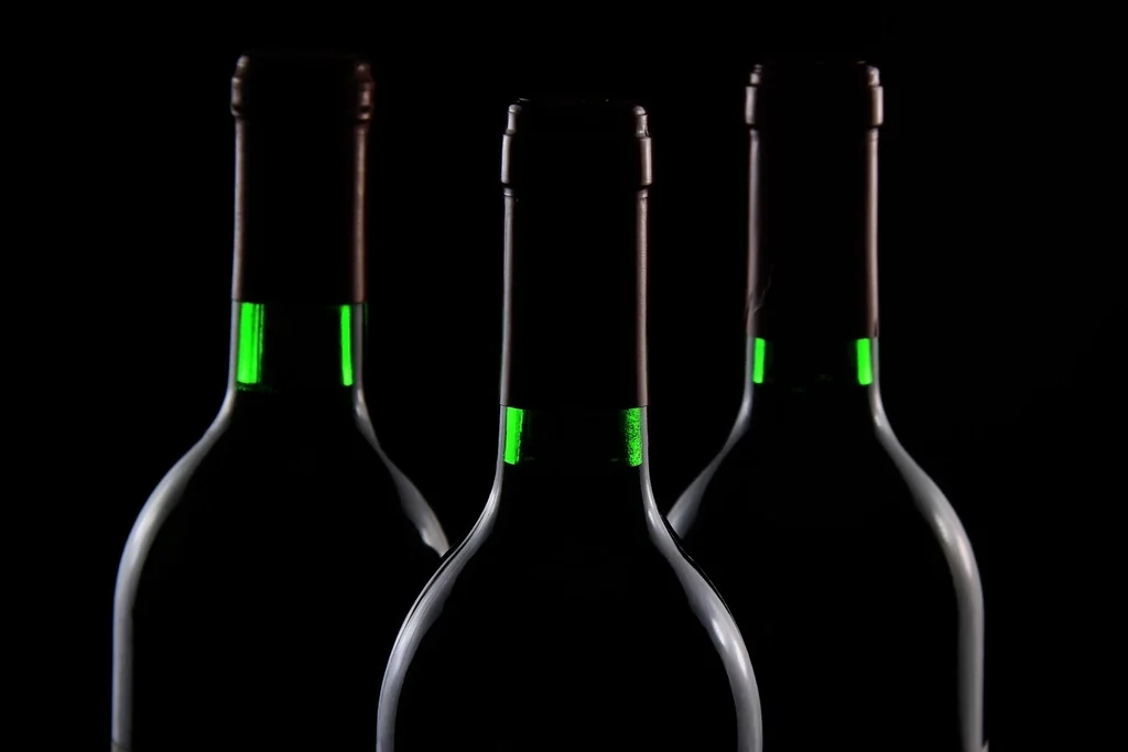 Trois bouteilles de vin fermées, cols alignés, sur fond sombre
