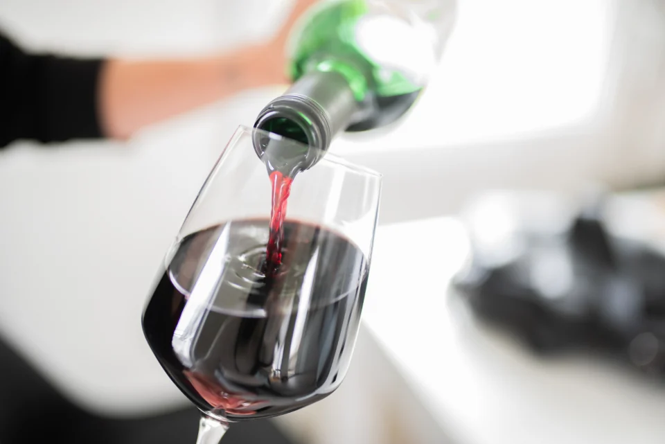Service d'un verre de vin rouge, bouteille inclinée au-dessus du verre